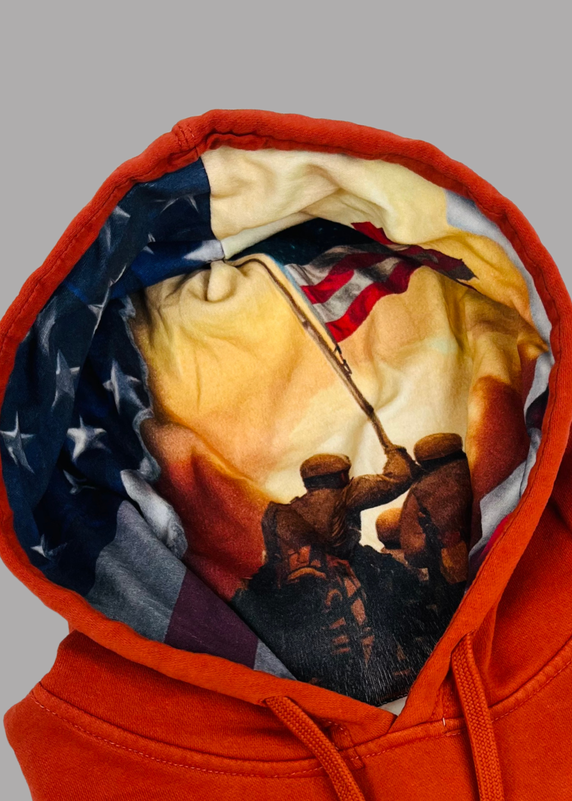 Red inner lined hoodie with a printed design of a solider holding an American flag on a gray background. American Flag. Patriotic. Jima. Raising the Flag on Iwo Jima. Honor. History. American Made. American Pride.