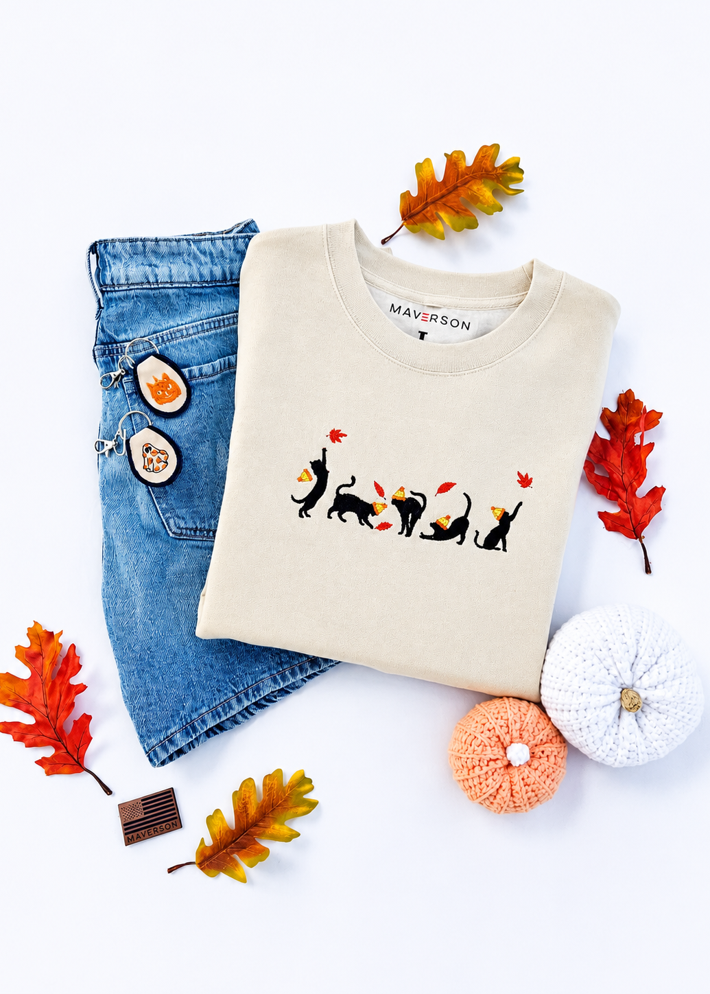 Beige sweatshirt with cat design, blue jeans, and autumn decorations on a white background