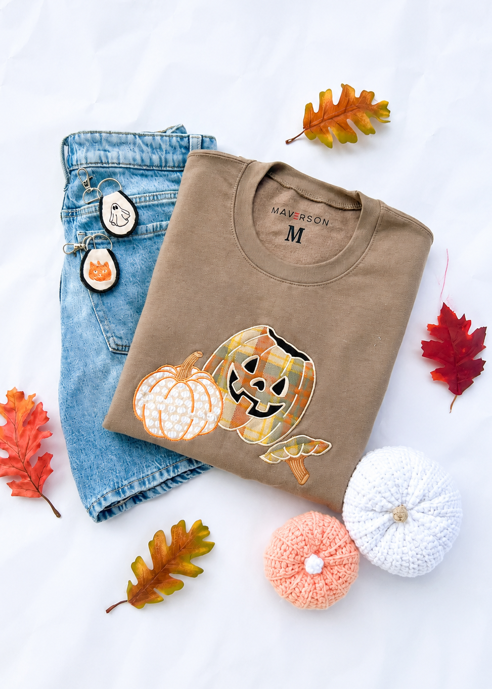 Folded brown t-shirt with pumpkin design, jeans, and decorative pumpkins on a white background