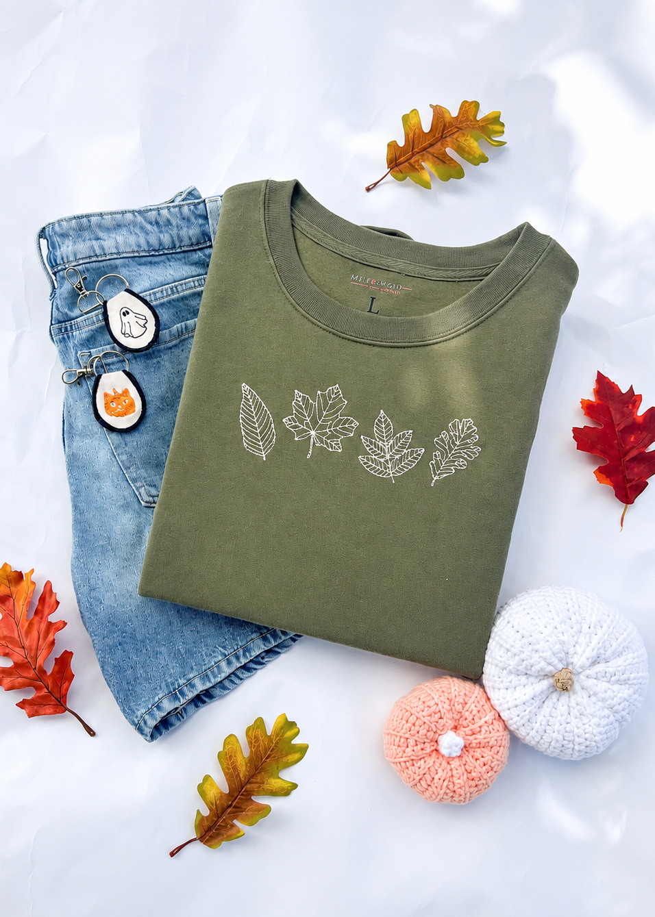 Folded green shirt with leaf design, jeans, and autumn leaves on a light background
