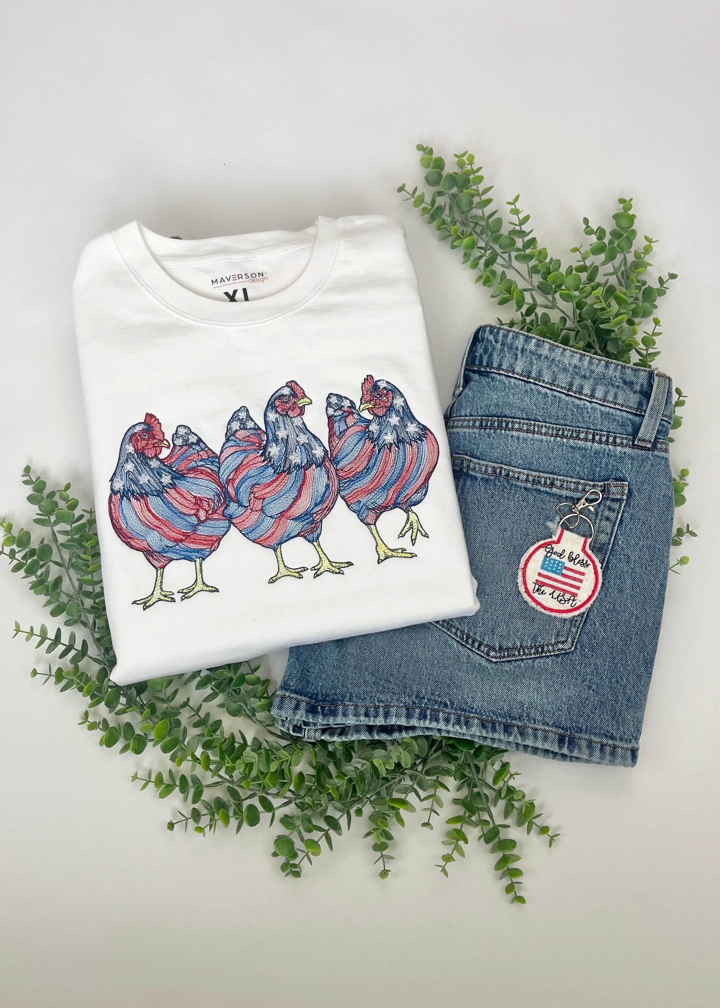 White t-shirt with colorful chicken design and blue jeans with a patch on a light gray background