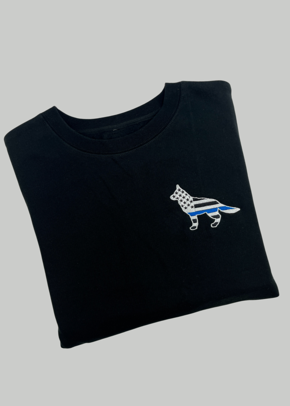 Folded black t-shirt with a small white dog logo on a gray background