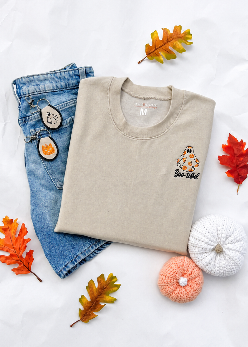 Folded beige sweatshirt with a ghost design, blue jeans, and decorative items on a white background
