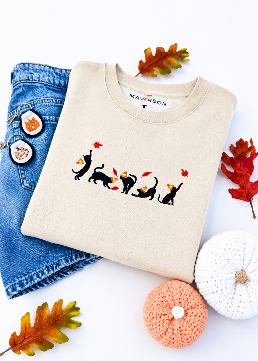 Beige sweatshirt with cat design, blue jeans, and decorative items on a white background