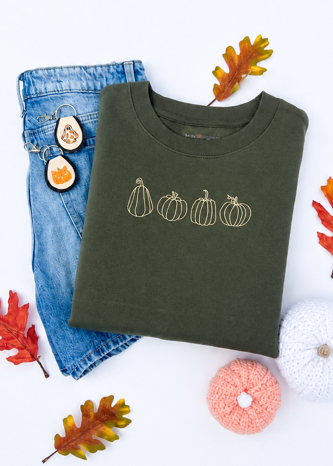 Green sweatshirt with pumpkin design, blue jeans, and decorative pumpkins on a white background