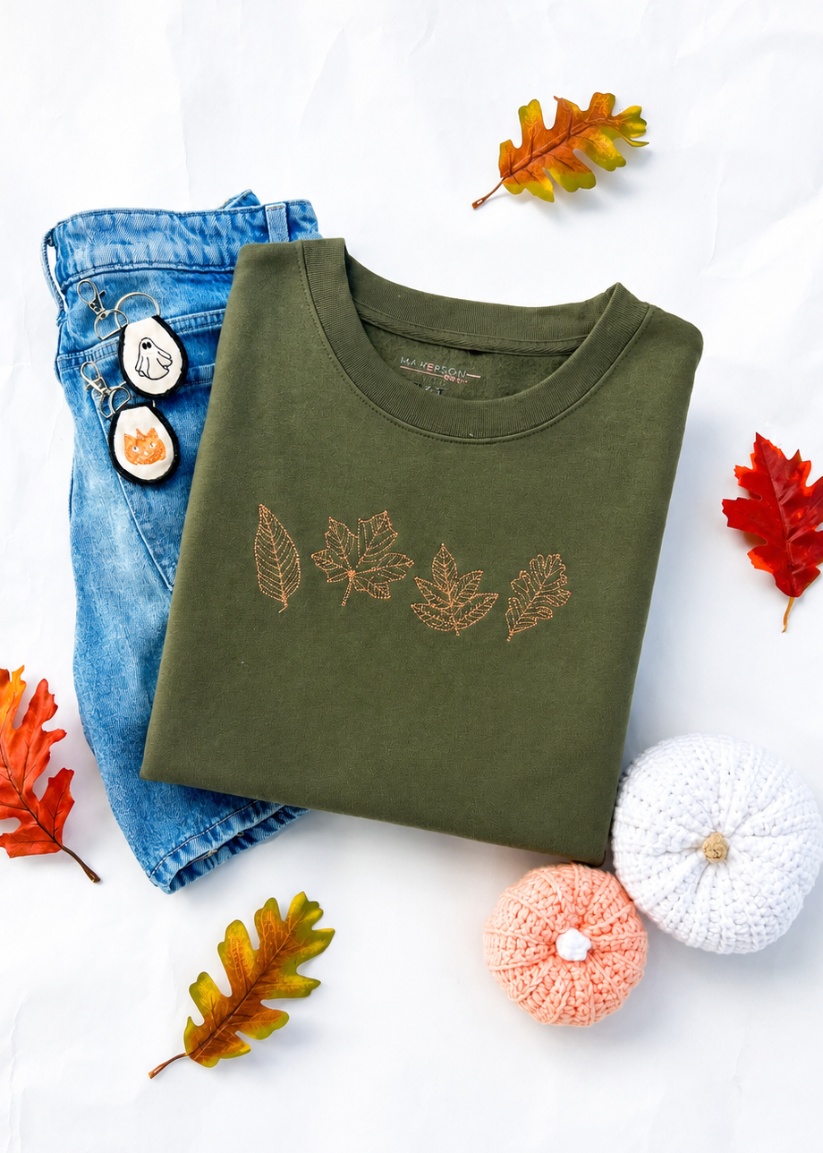 Green sweatshirt with leaf design, blue jeans, and decorative pumpkins on a white background