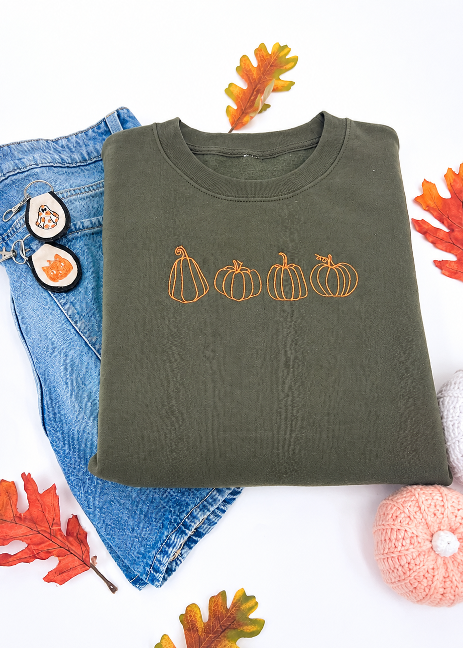Green sweatshirt with pumpkin design, blue jeans, and autumn leaves on a white background