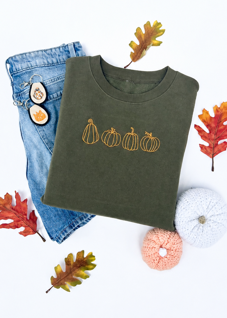 Green sweatshirt with pumpkin design, blue jeans, and decorative pumpkins on a white background
