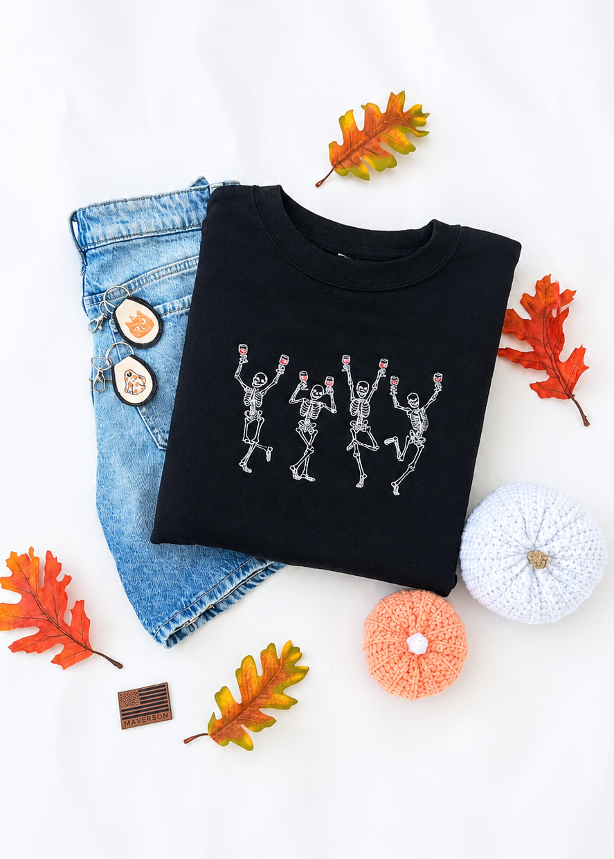 Black sweatshirt with skeleton dancing design, denim jeans, and autumn leaves on a white background