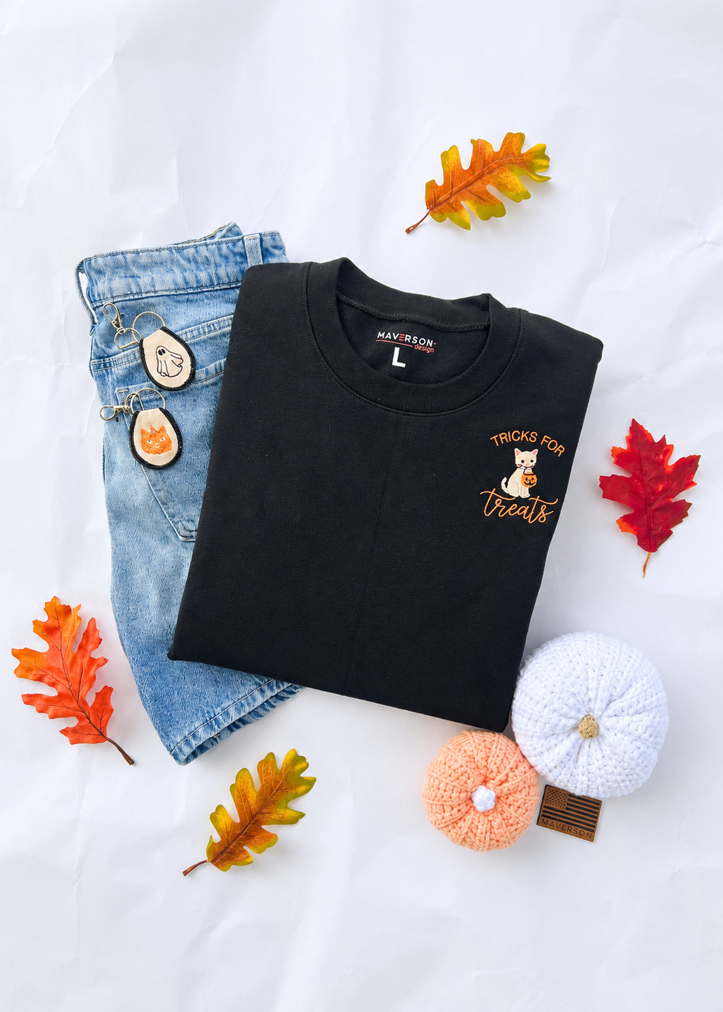 Black sweatshirt with 'Tricks for Treats' design, blue jeans, and decorative pumpkins on a white background.