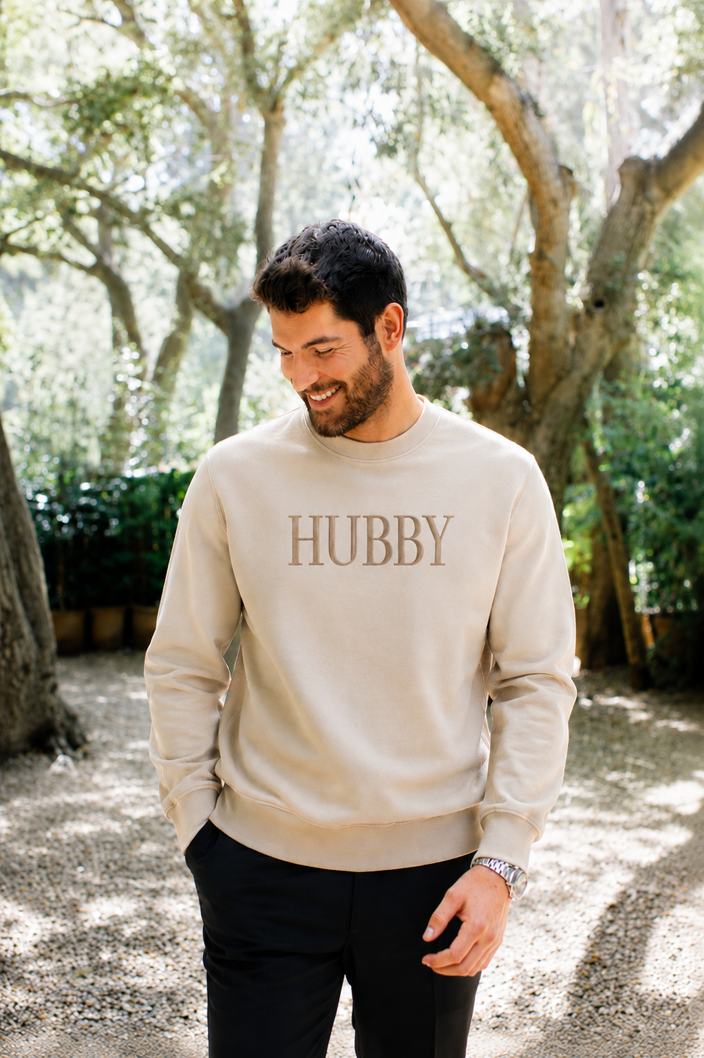 Man wearing a beige sweatshirt with 'HUBBY' text, standing outdoors among trees.