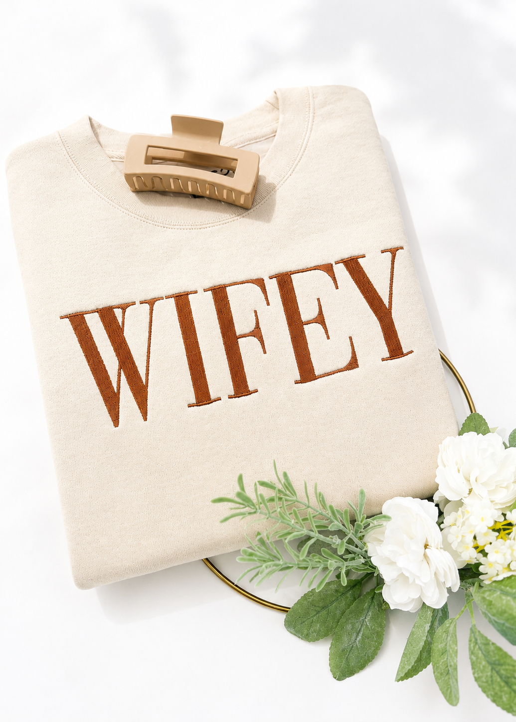 Beige sweatshirt with 'WIFEY' text on a white background with greenery and flowers.